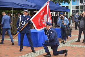 Zastępca Komendanta Głównego Policji trzyma sztandar. Komendant Powiatowy Policji w Tucholi klęka i całuje sztandar