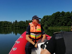 Dzielnicowy wspólnie ze strażą pożarną płynie łódką na jeziorze Bysławskim realizując zadania do akcji &quot;Kręci mnie bezpieczeństwo nad wodą&quot;.