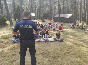 stojący policjant omawia harcerzom podstawowe zasady bezpieczeństwa podczas wakacji