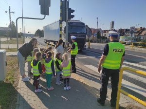 policjant tłumaczy dzieciom jak działa sygnalizacja świetlna przy przejściu dla pieszych