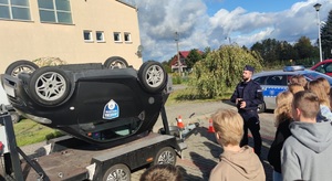 policjant stoi przy symulatorze dachowania i mówi o bezpieczeństwie podczas podróży