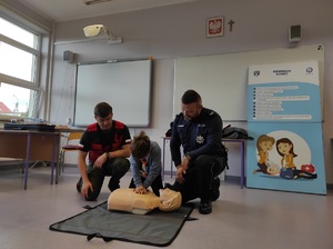 policjant i ratownik medyczny obserwują chłopca podczas ćwiczeń z pierwszej pomocy