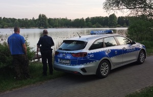 policjant i funkcjonariusz Służby Rybackiej stoją nad brzegiem wody