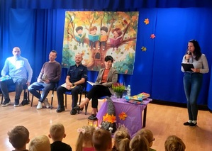 kobieta mówi do mikrofonu. Osoby siedzą na krzesłach