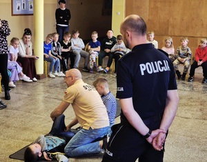 Policjant i strażak uczą dzieci udzielać pierwszej pomocy.